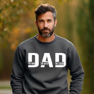 K&ouml;nnte beinhalten: Ein dunkelgraues Sweatshirt mit Rundhalsausschnitt und dem wei&szlig;en Schriftzug DAD in gro&szlig;en Gro&szlig;buchstaben. Unter jedem Buchstaben sind die W&ouml;rter THE MAN, THE MYTH und THE LEGEND in kleineren wei&szlig;en Gro&szlig;buchstaben mittig aufgedruckt.