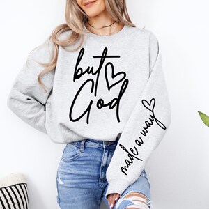 May include: A gray sweatshirt with the text "but God made a way" in black lettering. The text includes a cross and a heart.