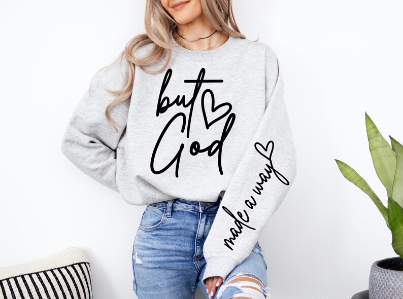 May include: A gray sweatshirt with the text "but God made a way" in black lettering. The text includes a cross and a heart.