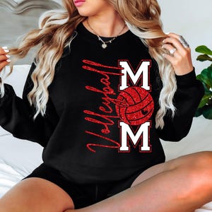 Peut inclure: Sweat-shirt noir avec l'inscription "Volleyball Mom" en paillettes rouges. Le mot "MOM" est en lettres blanches avec un graphisme de ballon de volley-ball rouge. Un haut d&eacute;contract&eacute; pour les fans de volley-ball.
