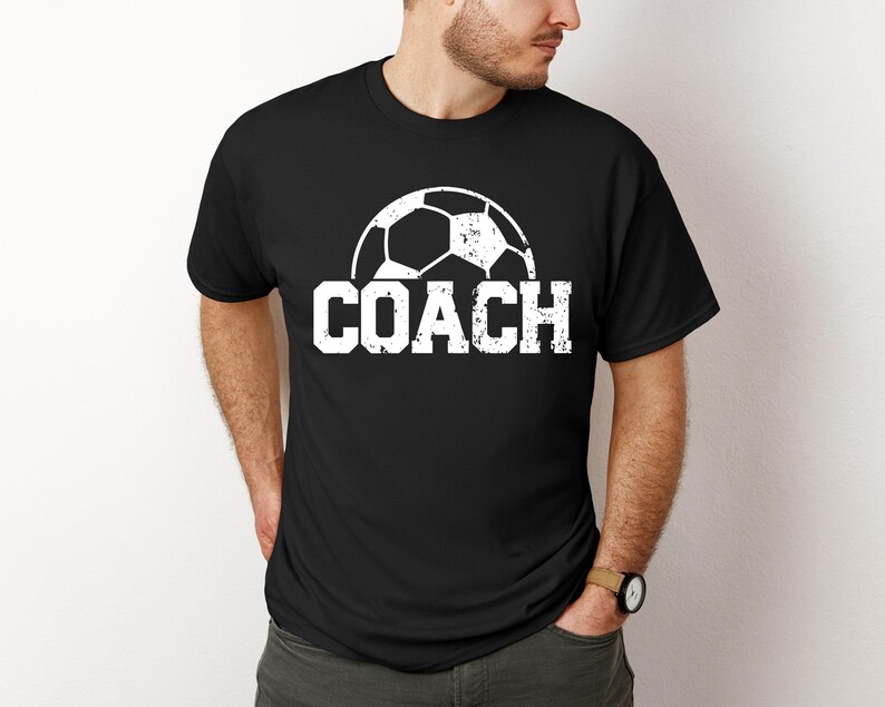 May include: Black t-shirt with a white soccer ball graphic and the word "COACH" in white distressed lettering.