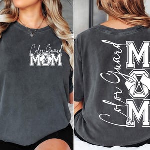 May include: A dark gray t-shirt with the text "Color Guard Mom" on the front and "Color Guard Mom" with a graphic of crossed flags on the back.