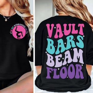 May include: Black sweatshirt with a graphic on the front that says "In My Gymnastics Era" and a silhouette of a gymnast doing a back handspring. The back of the sweatshirt has a graphic that says "Vault Bars Beam Floor" in a rainbow color scheme.