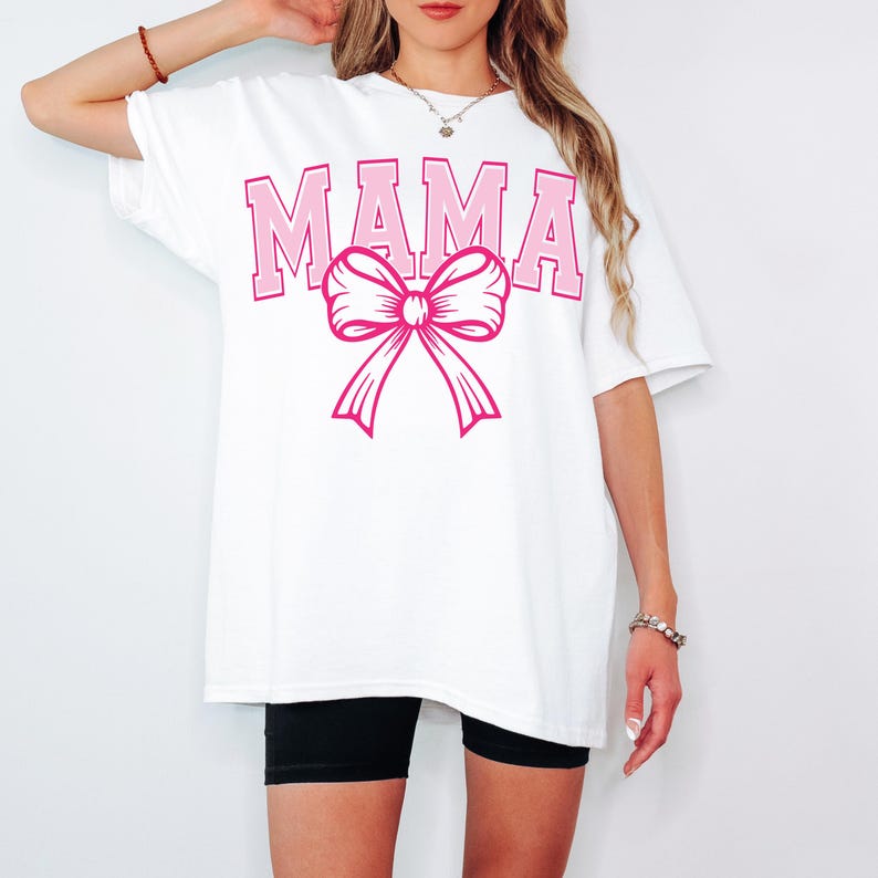 May include: White oversized t-shirt with the word "MAMA" in pink letters and a pink bow.