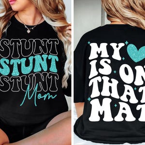 May include: Black sweatshirt with the words "STUNT STUNT STUNT Mom" in white and teal glitter lettering on the front. The back of the shirt says "MY HEART IS ON THAT MAT" with a teal glitter heart.