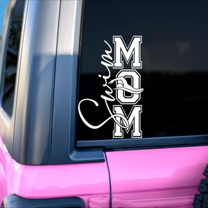 May include: A pink Jeep with a white vinyl decal on the back window that says "Swim Mom" with a stylized wave design.