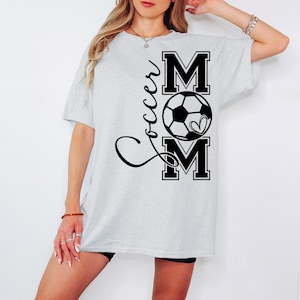 May include: A gray t-shirt with the text "Soccer Mom" in black lettering. The text is stylized with a soccer ball and a heart.