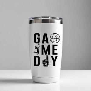 May include: White travel mug with a silver lid. The mug has the words "GAME DAY" in large black letters, a volleyball graphic, a volleyball player silhouette, and a number one foam finger.