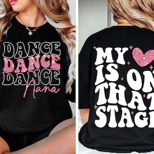 May include: Black sweatshirt with the words "DANCE DANCE DANCE Nana" in white and pink glitter lettering on the front. The back of the shirt says "MY HEART IS ON THAT STAGE" in white lettering with a pink glitter heart.