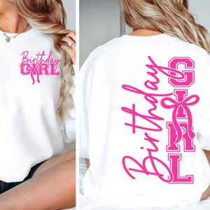 May include: White sweatshirt with the text "Birthday Girl" in pink script and block letters. The front features the text with a bow graphic. The back of the sweatshirt has the words "Birthday Girl" vertically with a bow graphic.