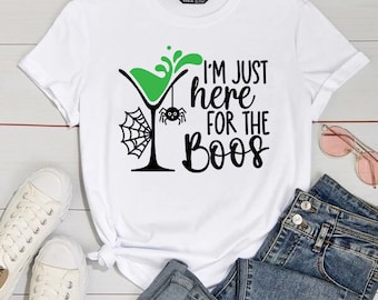 May include: White t-shirt with a green martini glass, a spider, and the text "I'm just here for the boos".