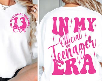 Puede incluir: Sudadera blanca con texto rosa que dice "In My Official Teenager Era" en la espalda y "In My Official Teenager Era 13" en el frente.