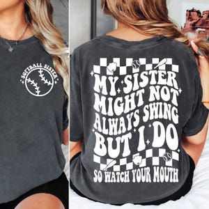 May include: Dark gray t-shirt with white text and softball graphics. The front of the shirt says "Softball Sister" around a softball graphic. The back says "My sister might not always swing but I do. So watch your mouth."