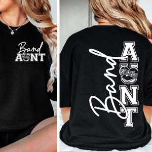 May include: Black sweatshirt with the text "Band Aunt" in white script and block letters. The front design includes a musical note and heart graphic. The back features the word "Band" vertically and the letters "AUNT" in a stacked design.