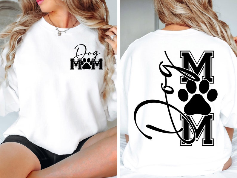Puede incluir: Sudadera blanca con el texto "Dog Mom" y una huella de pata en la parte delantera. La parte posterior de la sudadera tiene el texto "Dog Mom" con una huella de pata y una gran "M" en una fuente de estilo universitario.