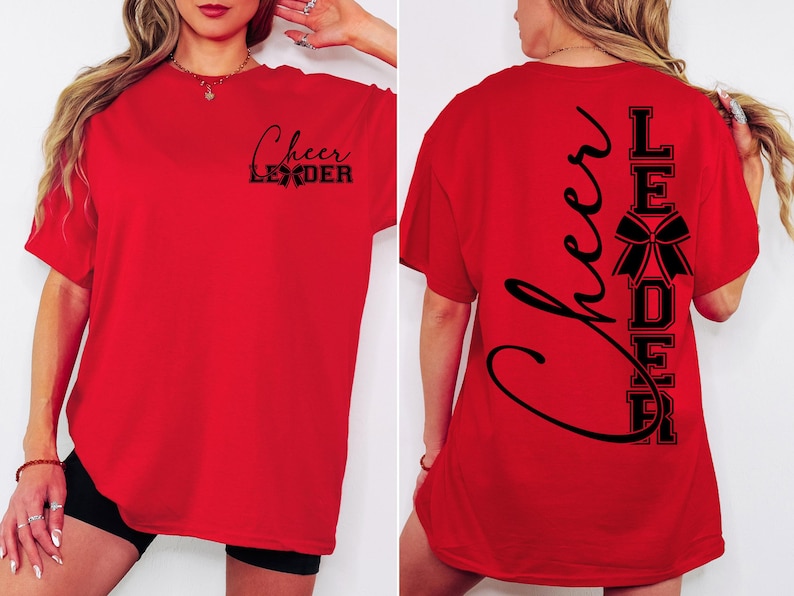 Puede incluir: Camiseta roja con el texto "Cheer Leader" en la parte delantera y el texto "Cheer Leader" con un lazo en la parte trasera.
