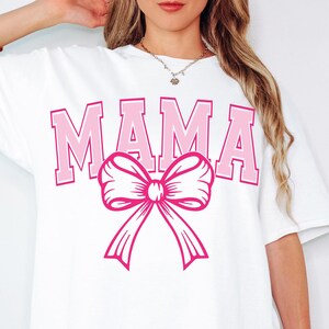 May include: White t-shirt with the word "MAMA" in pink letters and a pink bow.