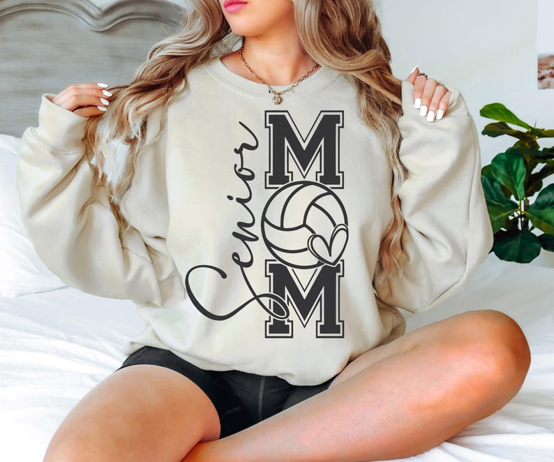 May include: A cream-colored sweatshirt with the words "Senior Mom" and a volleyball graphic printed on the front.