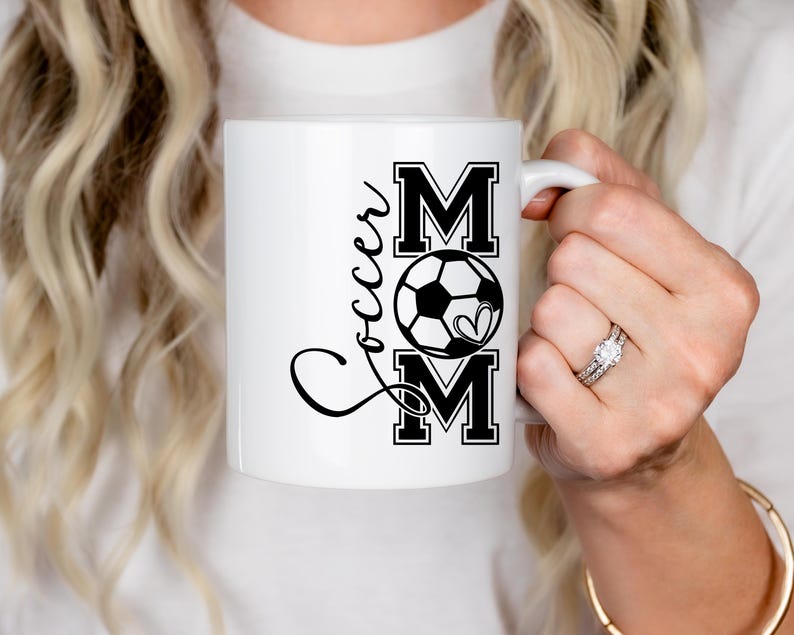 May include: White ceramic mug with a black and white design that says "Soccer Mom" with a soccer ball and heart graphic.