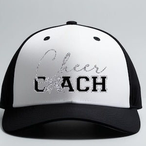 May include: A black and white baseball cap featuring the text "Cheer Coach" in silver glitter and black block letters. The cap has a curved peak and a mesh back, suitable for sports and outdoor activities.