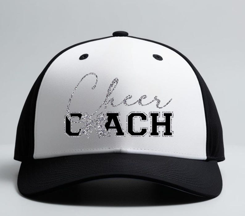 May include: A black and white baseball cap featuring the text "Cheer Coach" in silver glitter and black block letters. The cap has a curved peak and a mesh back, suitable for sports and outdoor activities.