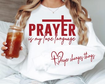 May include: White sweatshirt with red text that reads "PRAYER is my love language" and a red heart with a cross and the text "Prayer changes things".