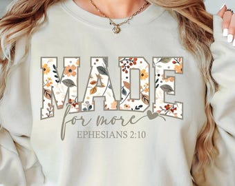 May include: Cream-colored sweatshirt with the words "MADE for more" in a floral design. The text "Ephesians 2:10" is below the main text. The floral design includes orange, brown, and gray leaves and flowers.