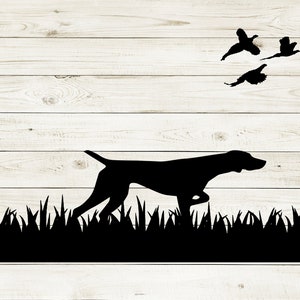 May include: Black silhouette of a dog pointing at a flock of birds flying in the air. The dog is standing in tall grass. The background is a white woodgrain surface.