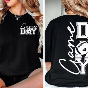 May include: Black sweatshirt with the words "Game Day" in white script and block letters, featuring a football graphic with a heart. The back of the shirt repeats the design vertically.