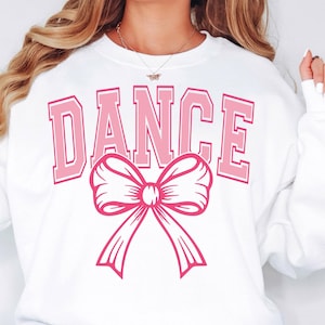 May include: White sweatshirt with the word "DANCE" in pink letters and a pink bow.