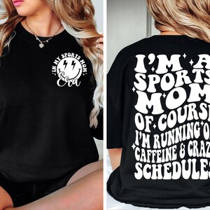 Pode incluir: Camiseta preta com texto branco que diz "Eu sou uma m&atilde;e esportiva, claro que estou correndo na cafe&iacute;na e em hor&aacute;rios loucos". A frente da camiseta tem um rosto sorridente branco com raios e o texto "Na minha era de m&atilde;e esportiva".