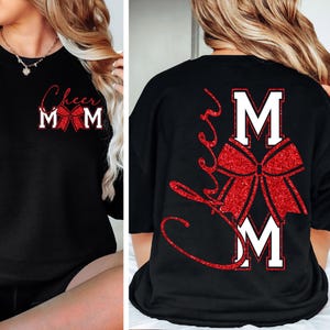 Peut inclure: Sweat-shirt noir avec l'inscription "Cheer Mom" en lettres cursives rouges et en lettres majuscules blanches. Un nœud rouge à paillettes est centré sous le texte. Le dos du t-shirt présente également le même motif.