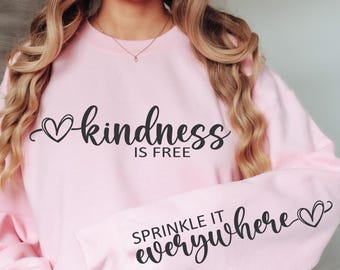 Può includere: Felpa rosa con la scritta "kindness is free" sul davanti e "sprinkle it everywhere" sulla manica, entrambe con un simbolo a forma di cuore.