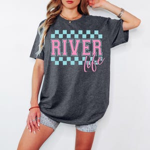 May include: A dark gray t-shirt with a pink and blue checkered pattern and the text "River Life" in pink.