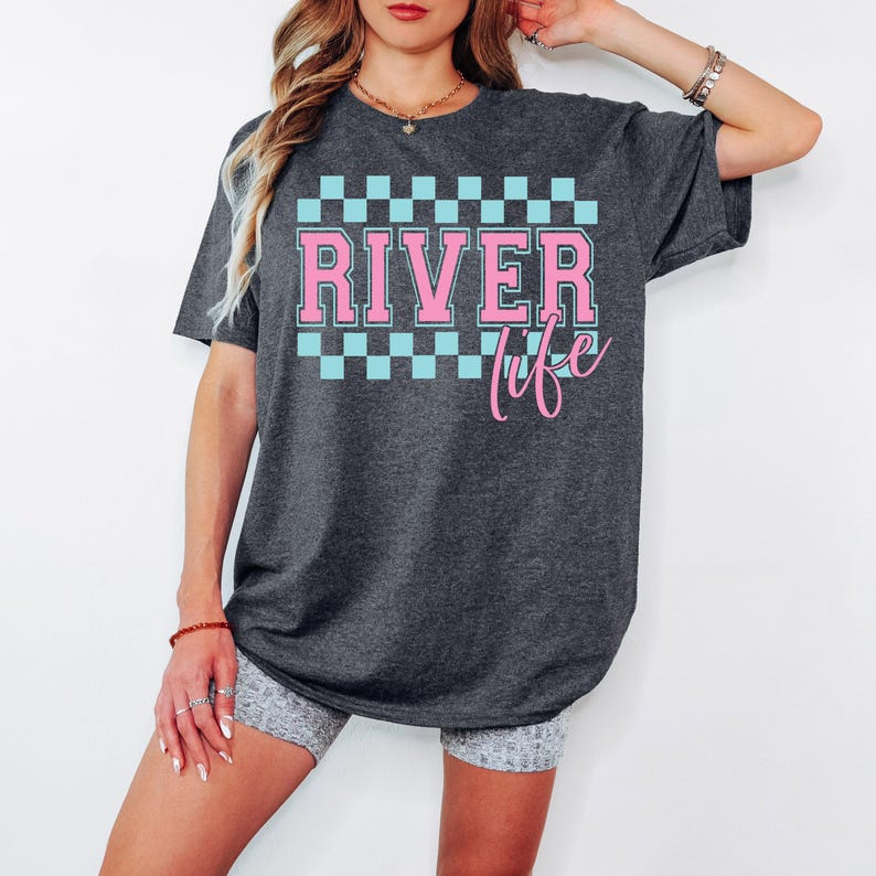May include: A dark gray t-shirt with a pink and blue checkered pattern and the text "River Life" in pink.