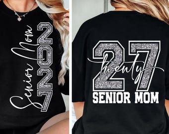 May include: A black t-shirt featuring white script text that reads Senior Mom and the year 2027 in silver glitter block numbers. The back of the shirt displays the large silver glitter numbers 27 with the word twenty in white script and Senior Mom.