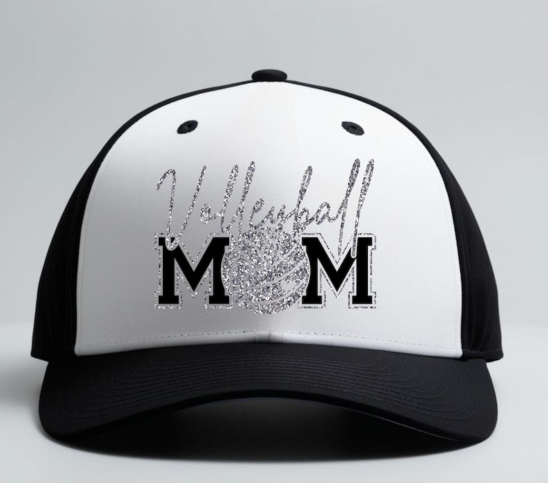 May include: A black and white baseball cap with the words "Volleyball Mom" in silver glitter script and block letters. A silver glitter volleyball is in the center of the word "Mom". The cap has a black brim and a white front panel.