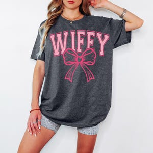 May include: A dark gray oversized t-shirt with the word "WIFFY" printed in pink letters with a pink bow underneath.