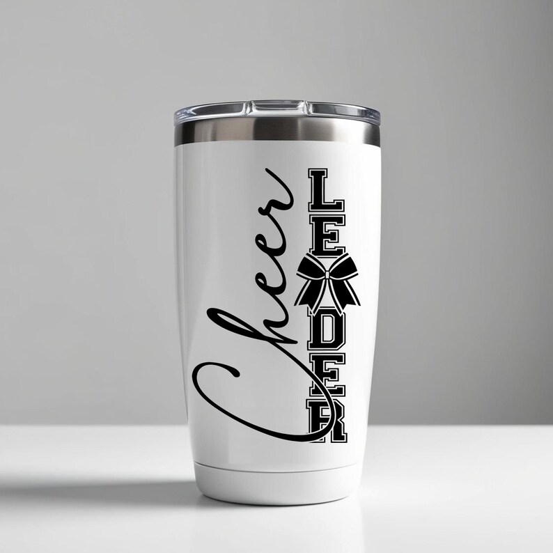 Puede incluir: Un vaso de acero inoxidable blanco con un dise&ntilde;o negro que dice "Cheer Leader" con un lazo negro en el medio de la palabra "Leader".