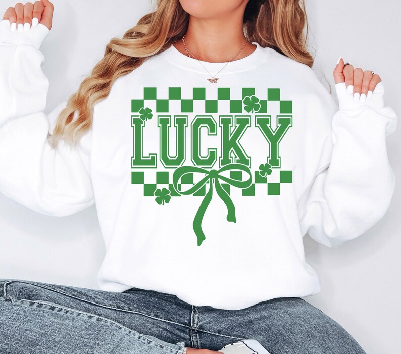 Pu&ograve; includere: Felpa bianca con un motivo a scacchi verdi e la parola "LUCKY" in lettere verdi. Un fiocco verde &egrave; centrato sotto la parola.