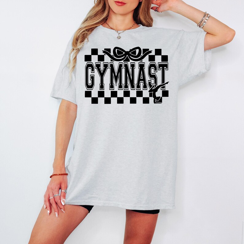May include: A gray oversized t-shirt with a black and white checkered design and the text "GYMNAST" in black. A black silhouette of a gymnast is in the design.