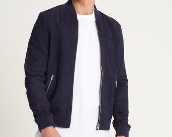 May include: A navy blue bomber jacket with a ribbed collar and cuffs. The jacket features a zip-up front and two side pockets. The material looks like suede or a suede-like fabric. The jacket is worn over a white t-shirt.
