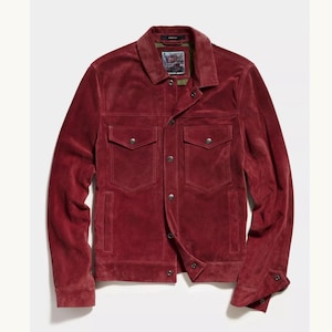 May include: A burgundy suede jacket with a classic design. It features a collared neckline, two chest pockets with button closures, and buttoned cuffs. The jacket has a button-up front and a tailored fit, suitable for a stylish appearance.