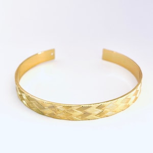 Może przedstawiać: Złota bransoletka typu bangle z plecionym wzorem.