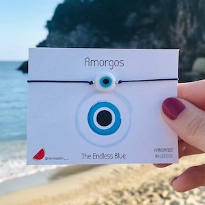 Peut inclure: Un bracelet avec un charme bleu et blanc en forme de mauvais œil sur une ficelle bleue. Le bracelet est sur une carte blanche avec le texte "Amorgos The Endless Blue Handmade in Greece".