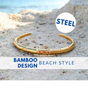 May include: A gold-toned steel bracelet with a bamboo design. The bracelet is on a sandy beach with the word "STEEL" in a blue circle above it. The text "BAMBOO DESIGN BEACH STYLE" is below the bracelet.