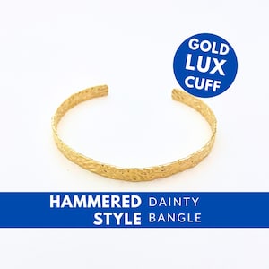 Op de afbeelding: Een goudkleurige gehamerde manchetarmband. De armband heeft een getextureerd oppervlak en is aan de uiteinden open. De afbeelding bevat de tekst "GOLD LUX CUFF" in een blauwe cirkel en "HAMMERED DAINTY STYLE BANGLE" in een blauwe banner.