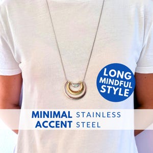 Könnte beinhalten: Eine lange, minimalistische Halskette mit drei halbmondförmigen Anhängern in Silber, Gold und Hellblau-Grün. Die Halskette hängt an einer filigranen Silberkette. Der Text auf dem Bild lautet "MINIMAL STAINLESS ACCENT STEEL" und "LONG MINDFUL STYLE."
