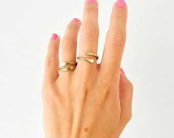 May include: Two gold rings on a hand with pink nail polish. The rings are simple and delicate, with one ring being a thin band and the other a slightly thicker band with a curved design.