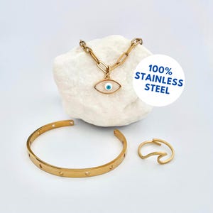 Könnte beinhalten: Goldfarbenes Schmuckset mit einer Halskette mit einem Augenanhänger, einem Armband mit kreisförmigen Ausschnitten und einem ringförmigen Ring. Die Halskette hat ein Kettenglied-Design. Der Augenanhänger hat einen weißen Hintergrund mit einem blauen Augendesign.